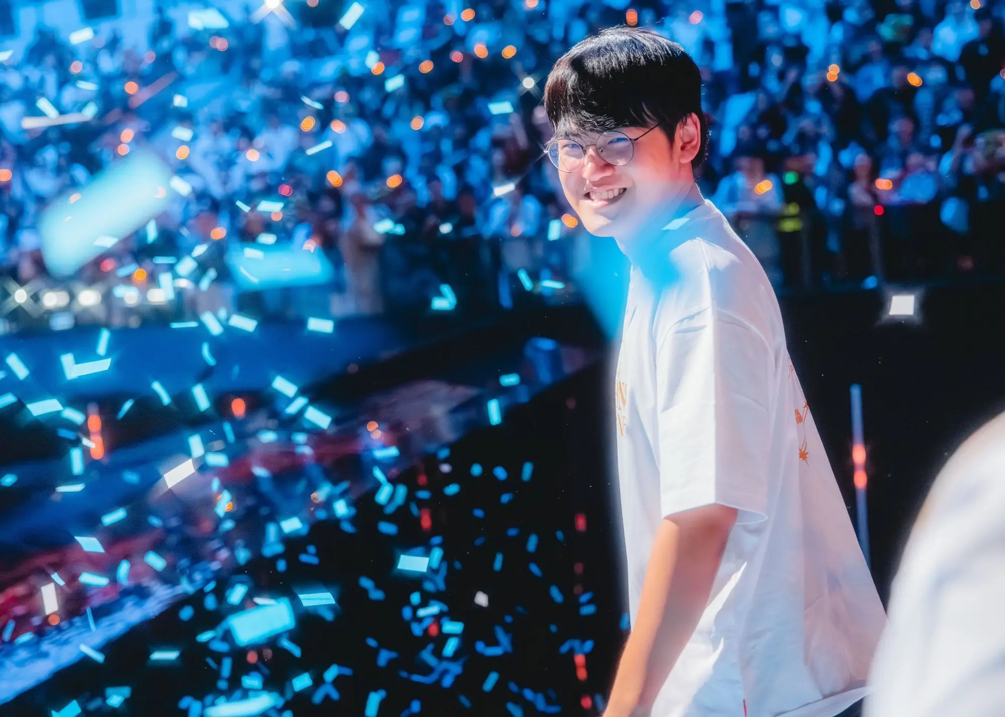 Gumayusi mỉm cười trên sân khấu với ánh đèn và pháo hoa giấy